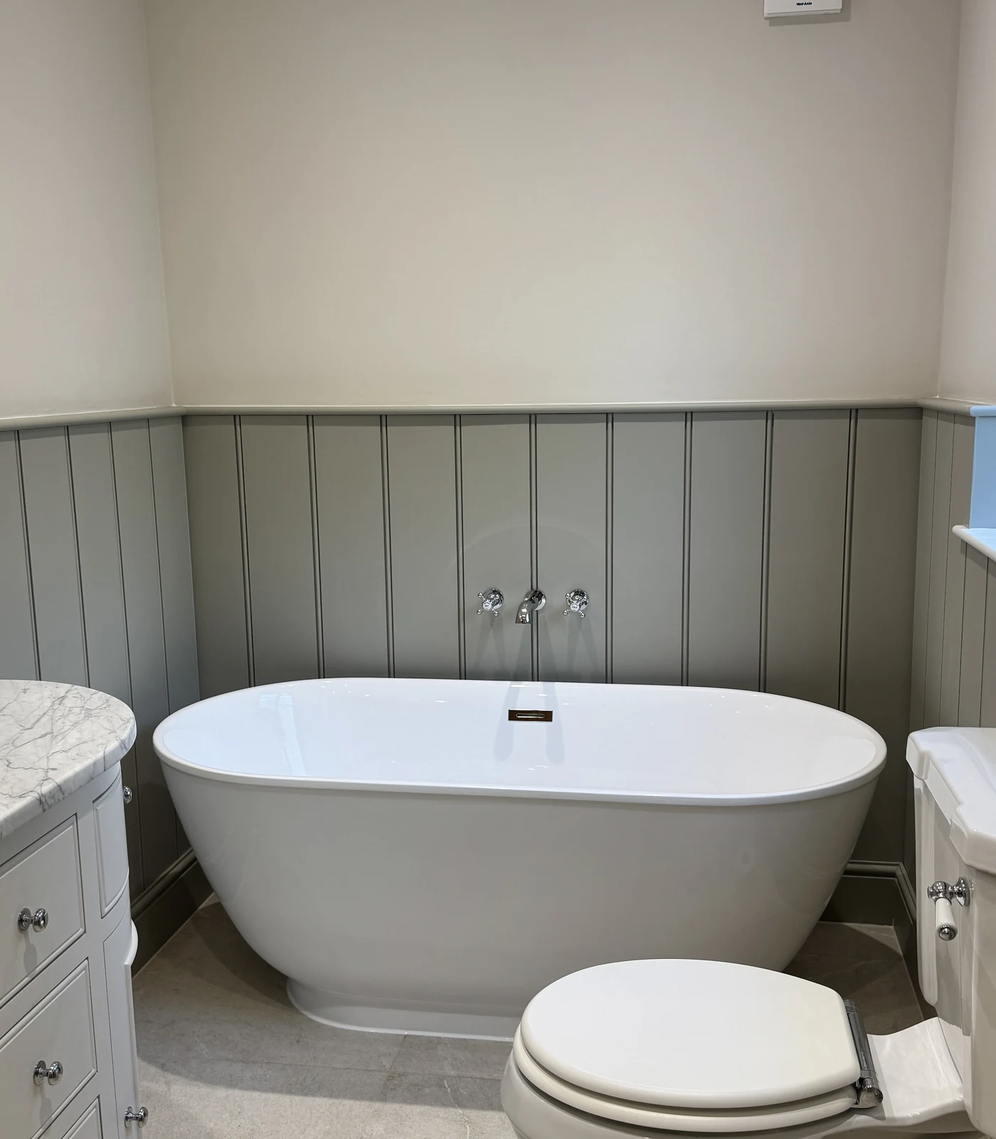 Freestanding bath against sage tongue-and-groove panelling, bathroom renovation