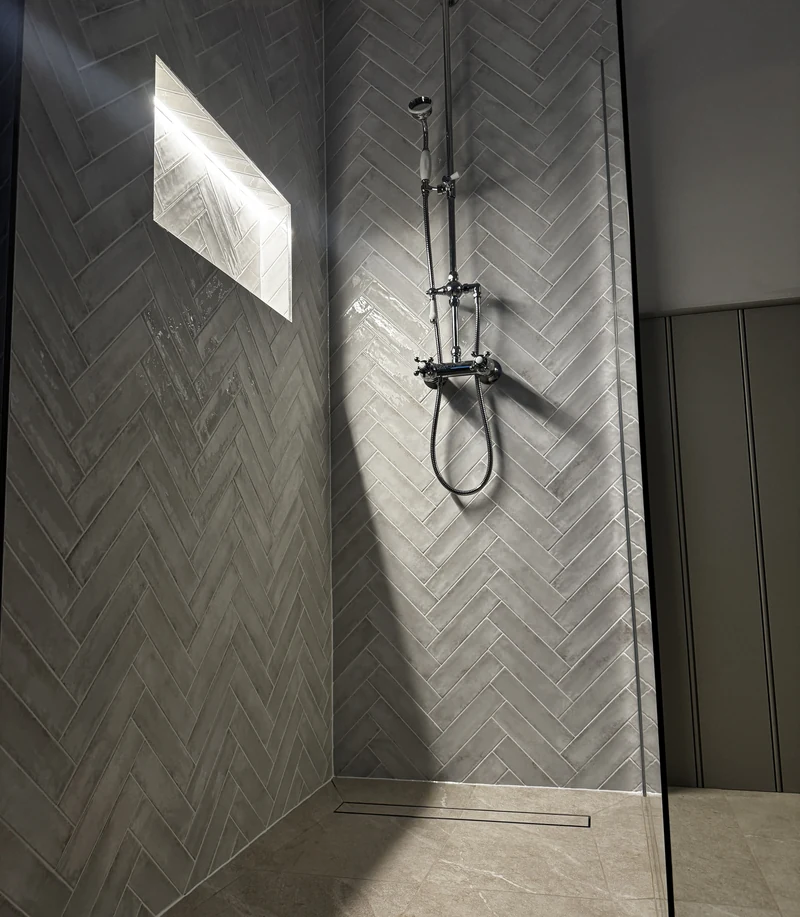 Herringbone-tiled walk-in shower with a lit niche