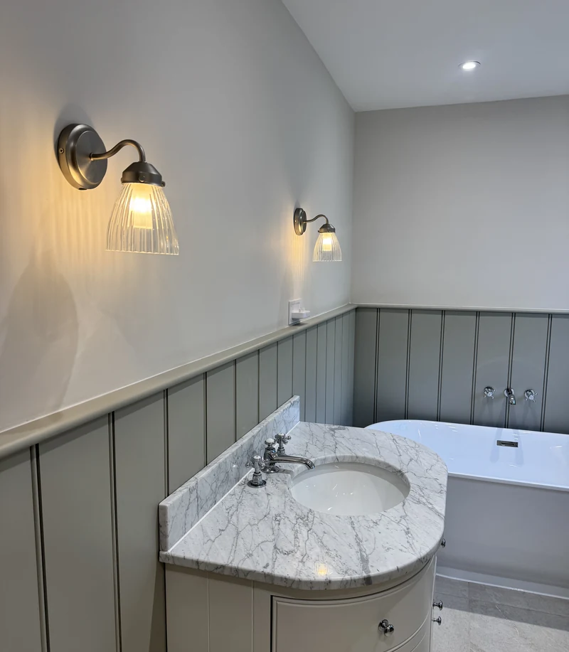 Marble-topped vanity and freestanding bath under ribbed wall lights