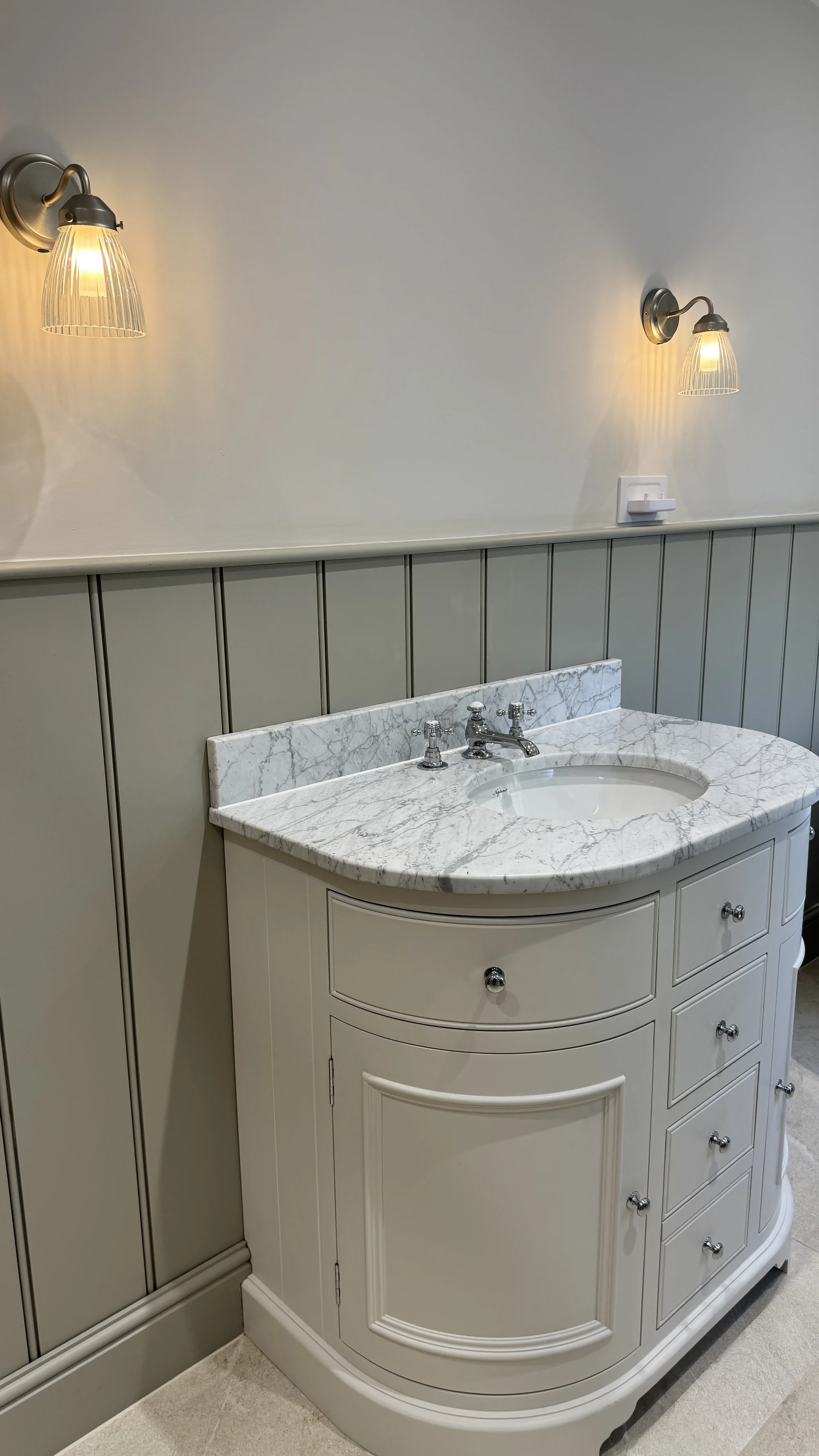 Curved vanity with a marble top and ribbed wall light