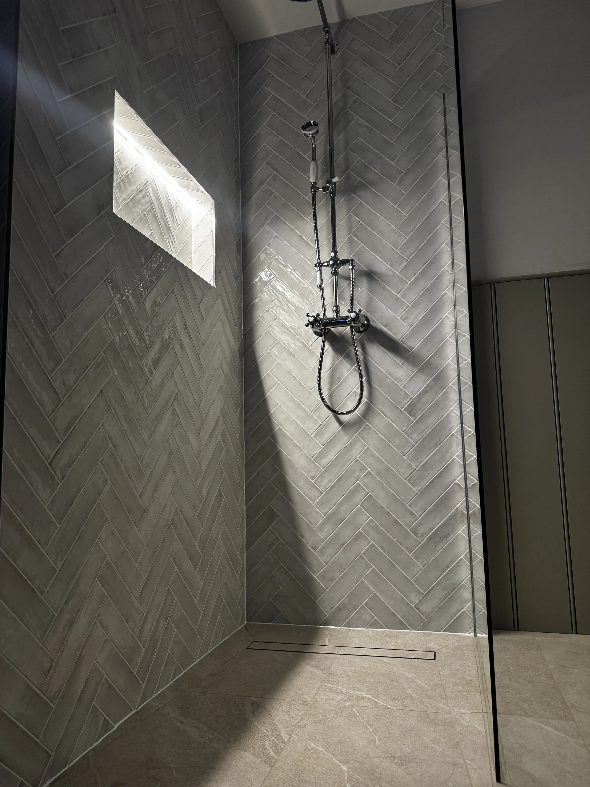 Walk-in shower lined in herringbone stone-look tile with a lit niche