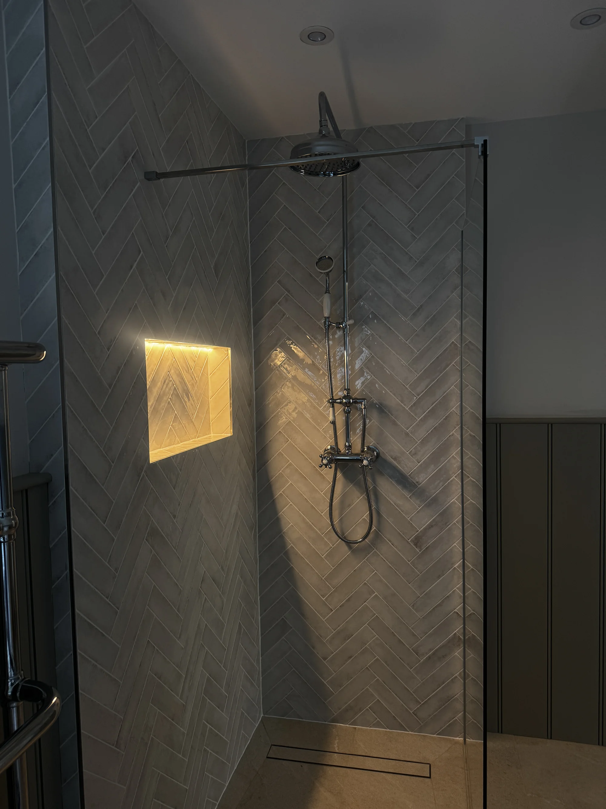Exposed thermostatic shower against herringbone tiling