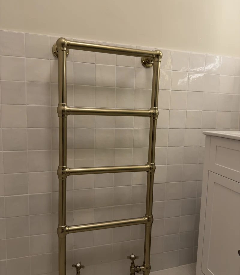 Traditional brass heated towel rail on handmade-look tiling