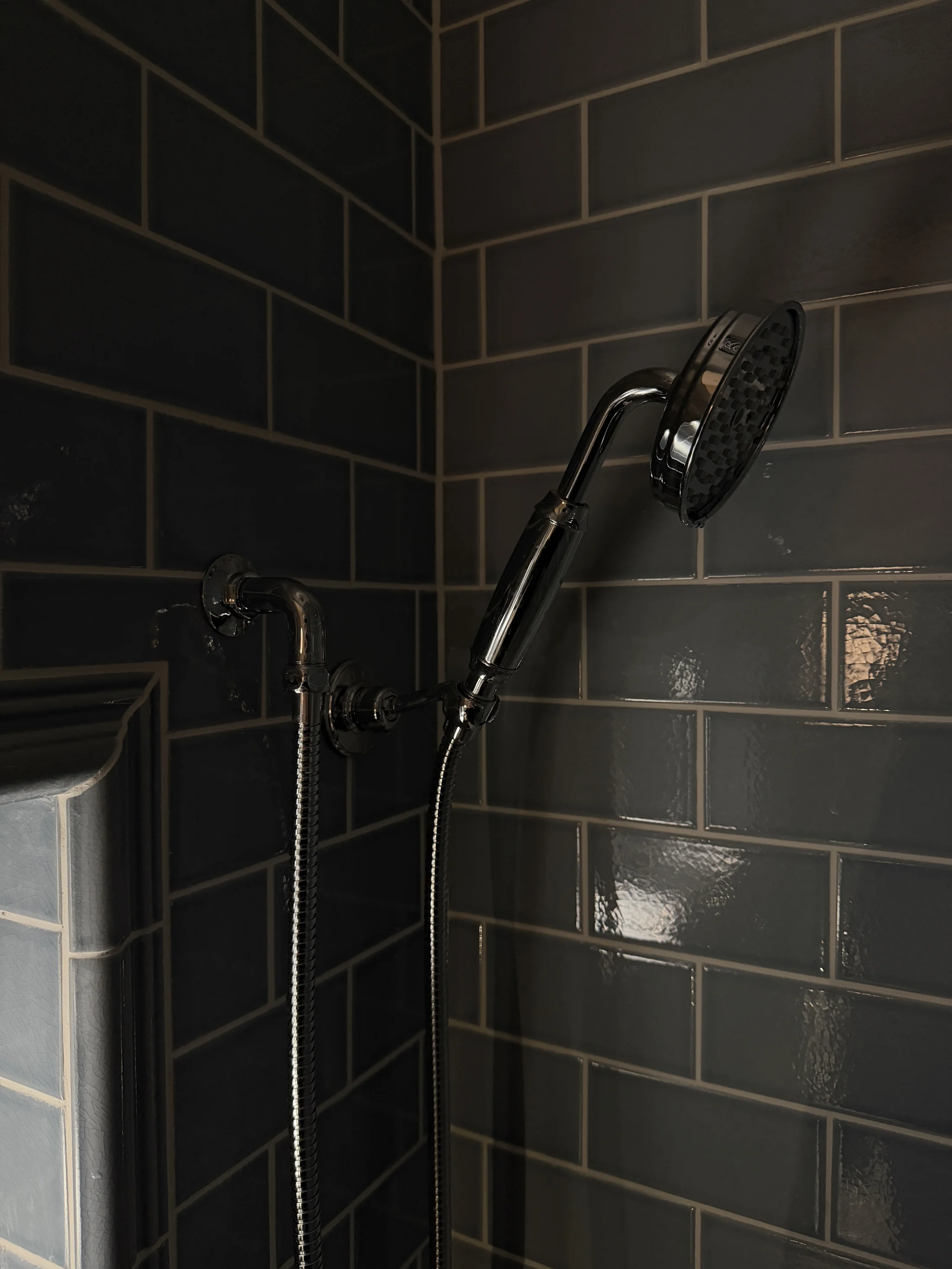 Chrome shower handset and hose on dark tiling, St Albans
