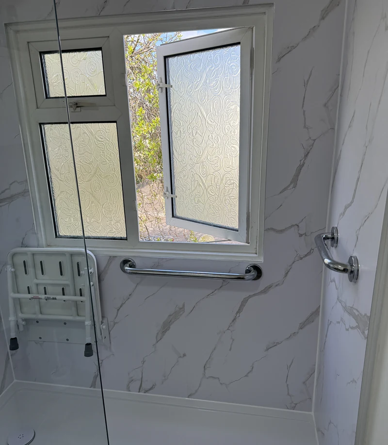 Fold-down shower seat and grab rail beside the window, accessible bathroom Hertfordshire