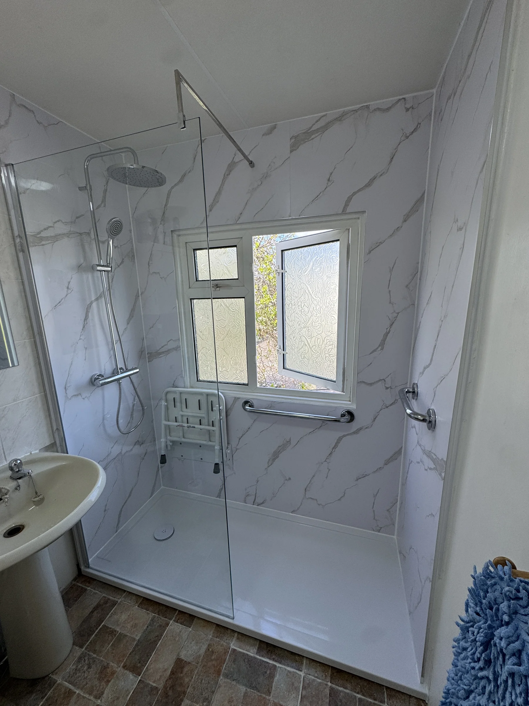 Accessible bathroom with level-access shower and marble-effect panelling, Hertfordshire