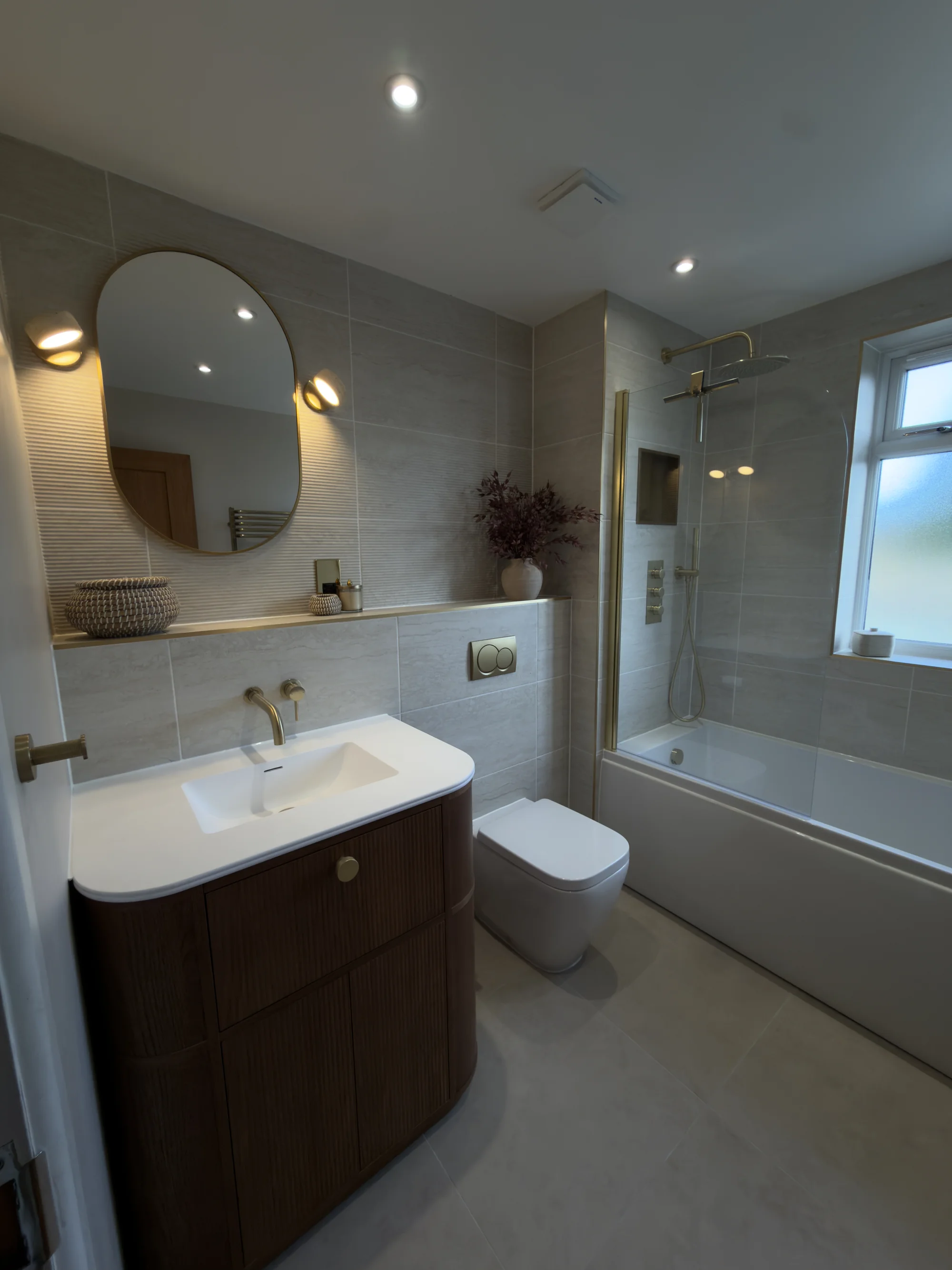 Bathroom renovation with a walnut vanity, oval mirror and stone tiling