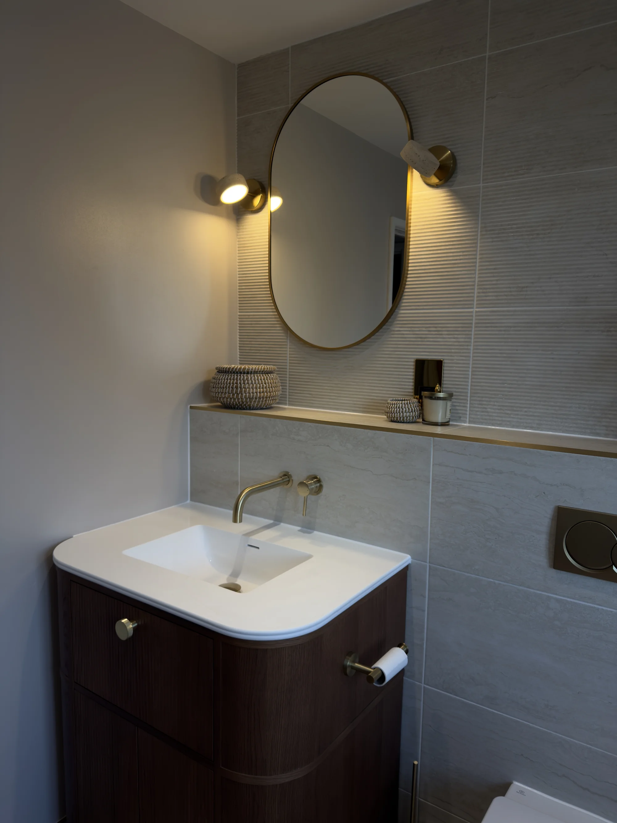 Oval mirror and brass wall lights above the walnut vanity