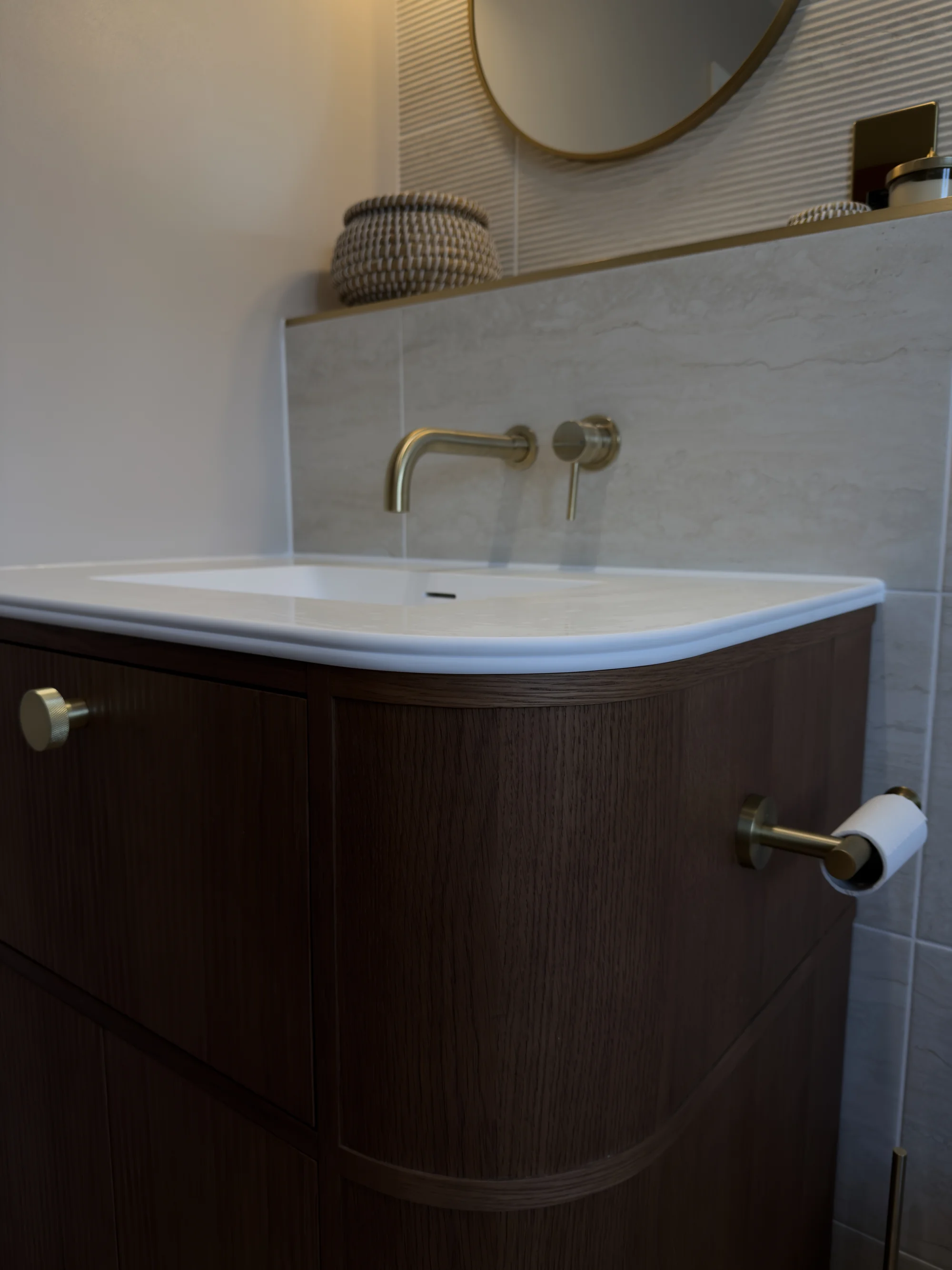 Wall-mounted brass taps and curved countertop basin